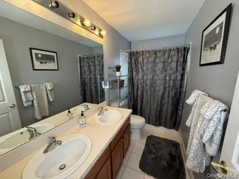 Bathroom featuring double vanity, light tile patterned floors, and shower / tub combo with curtain Bathroom featuring double vanity, light tile patterned floors, and shower / tub combo with curtain