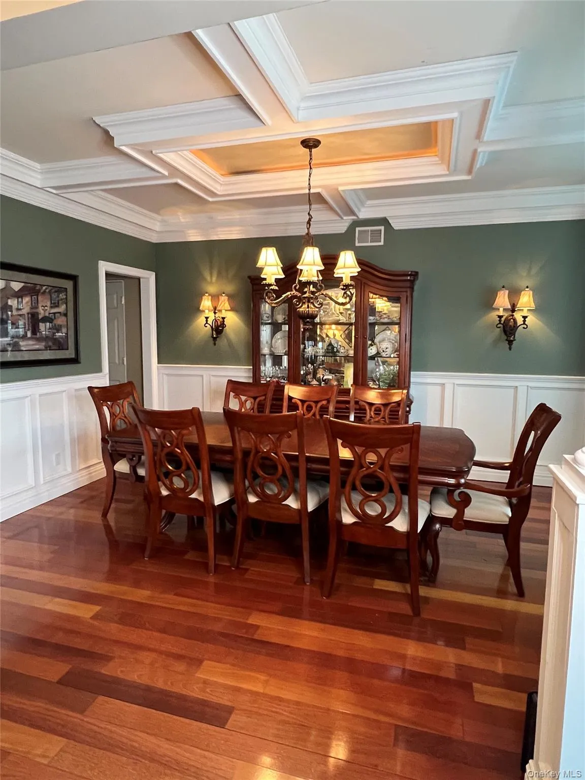 Dining space with suspended lighting, a wainscoted wall, wood finished floors, coffered ceiling, and crown molding Dining space with suspended lighting, a wainscoted wall, wood finished floors, coffered ceiling, and crown molding