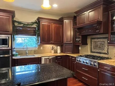Kitchen with dark stone countertops, stainless steel appliances, and backsplash Kitchen with dark stone countertops, stainless steel appliances, and backsplash