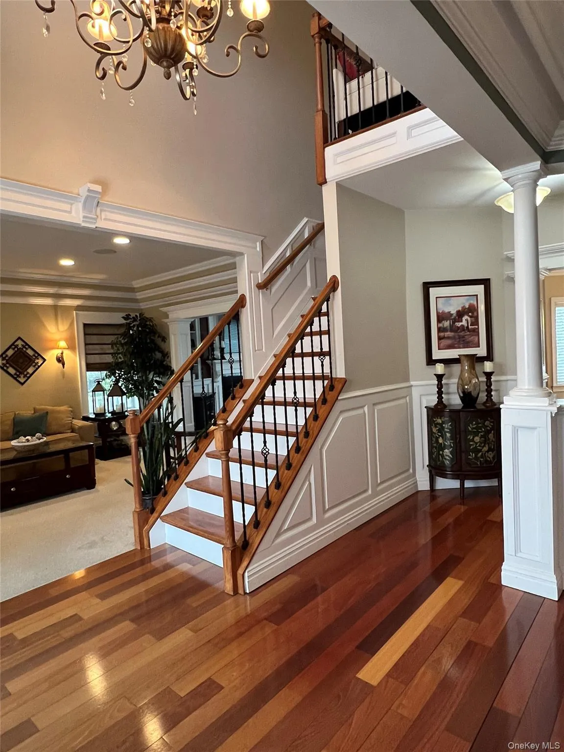 Staircase with a decorative wall, a wainscoted wall, wood-type flooring, a chandelier, and ornamental molding Staircase with a decorative wall, a wainscoted wall, wood-type flooring, a chandelier, and ornamental molding