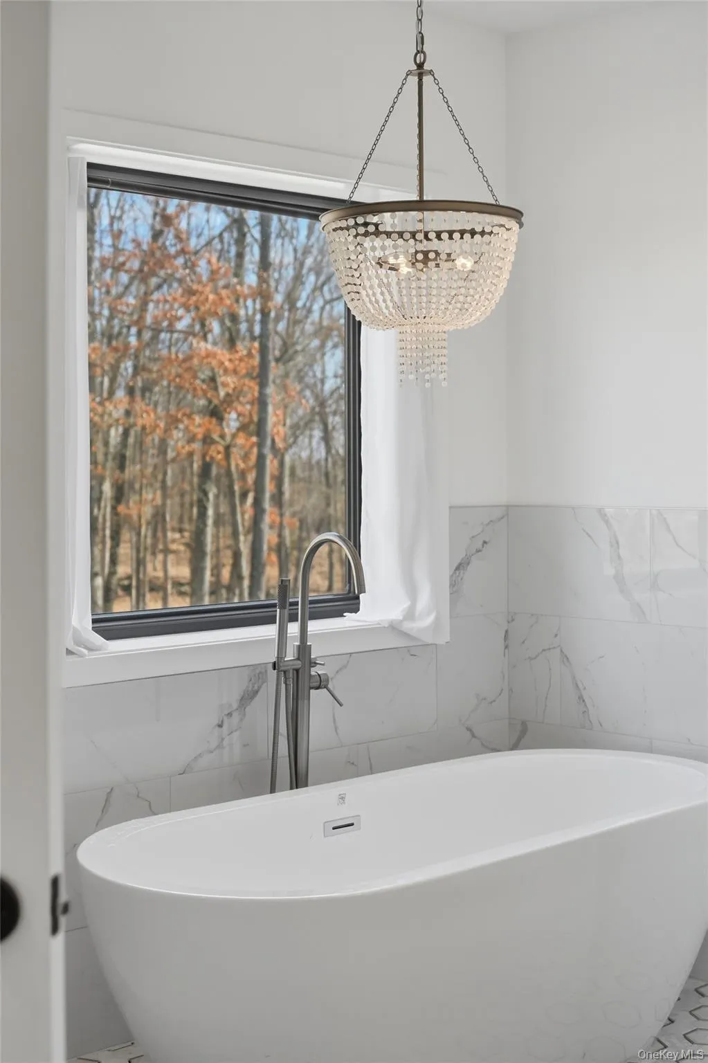 Spa-like soaking tub in the ensuite bathroom with elegant light fixture and luxurious tile Spa-like soaking tub in the ensuite bathroom with elegant light fixture and luxurious tile