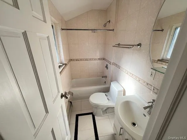 Full bathroom featuring sink, tile patterned floors, shower / bath combination, vaulted ceiling, and tile walls Full bathroom featuring sink, tile patterned floors, shower / bath combination, vaulted ceiling, and tile walls