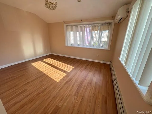 Spare room featuring hardwood / wood-style flooring, a baseboard radiator, a wall unit AC, and vaulted ceiling Spare room featuring hardwood / wood-style flooring, a baseboard radiator, a wall unit AC, and vaulted ceiling