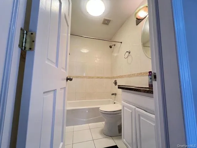Full bathroom with tile patterned flooring, vanity, tiled shower / bath combo, and toilet Full bathroom with tile patterned flooring, vanity, tiled shower / bath combo, and toilet