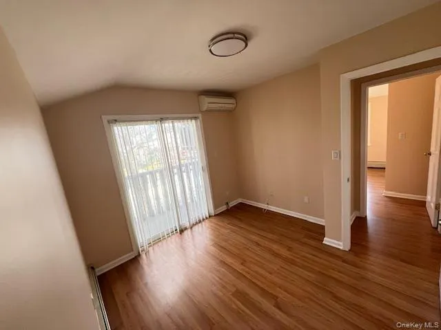 Empty room featuring vaulted ceiling, dark hardwood / wood-style floors, and a wall mounted air conditioner Empty room featuring vaulted ceiling, dark hardwood / wood-style floors, and a wall mounted air conditioner