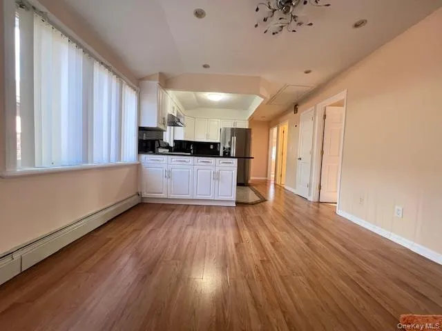 Kitchen with stainless steel refrigerator, white cabinetry, a baseboard radiator, light hardwood / wood-style flooring, and vaulted ceiling Kitchen with stainless steel refrigerator, white cabinetry, a baseboard radiator, light hardwood / wood-style flooring, and vaulted ceiling