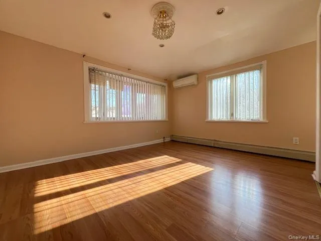 Spare room with a wall mounted air conditioner, wood-type flooring, and baseboard heating Spare room with a wall mounted air conditioner, wood-type flooring, and baseboard heating