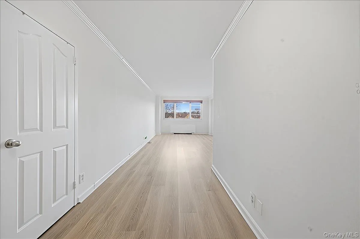 Corridor with light wood finished floors and crown molding heading from entry way into living/dining area. Corridor with light wood finished floors and crown molding heading from entry way into living/dining area.