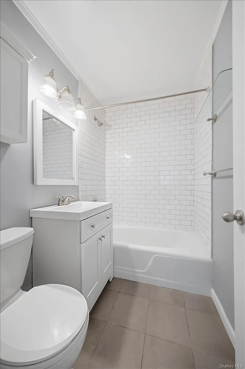 Full bathroom with vanity, washtub / shower combination, ornamental molding, and light tile patterned flooring Full bathroom with vanity, washtub / shower combination, ornamental molding, and light tile patterned flooring