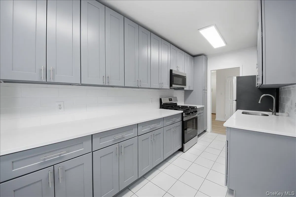 Kitchen with gray cabinets, stainless steel appliances, light stone countertops, tasteful backsplash, and light tile patterned flooring Kitchen with gray cabinets, stainless steel appliances, light stone countertops, tasteful backsplash, and light tile patterned flooring