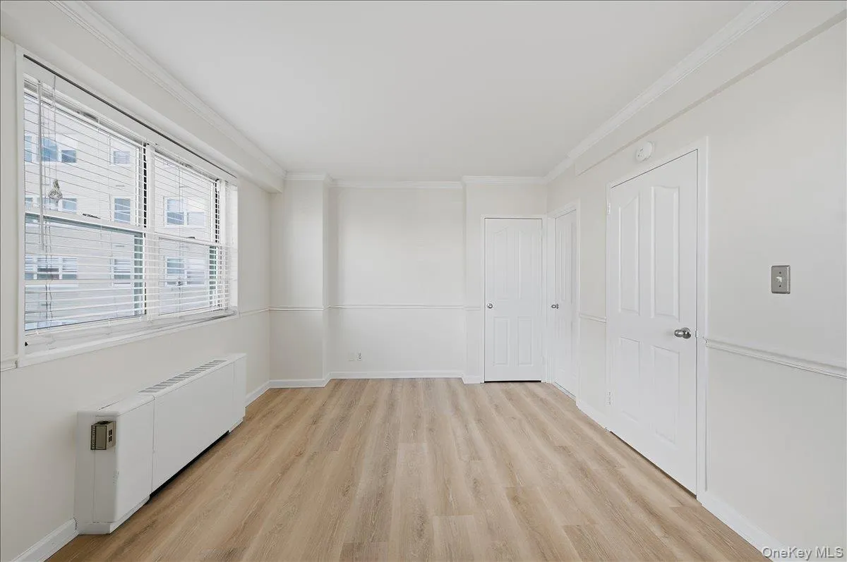 Unfurnished primary bedroom with radiator heating unit, crown molding, and light wood-type flooring Unfurnished primary bedroom with radiator heating unit, crown molding, and light wood-type flooring