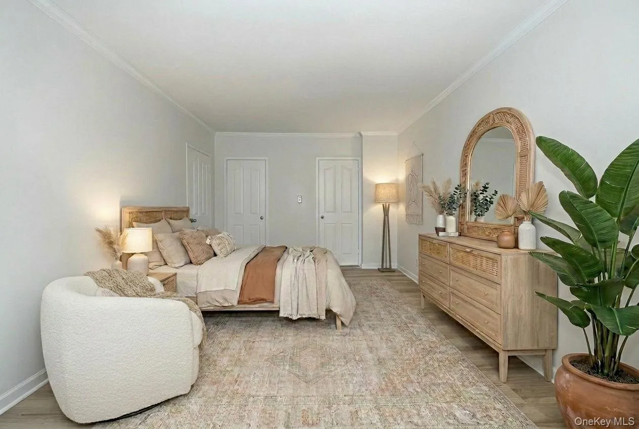 Staged bedroom with light wood-style floors, multiple closets, and ornamental molding Staged bedroom with light wood-style floors, multiple closets, and ornamental molding