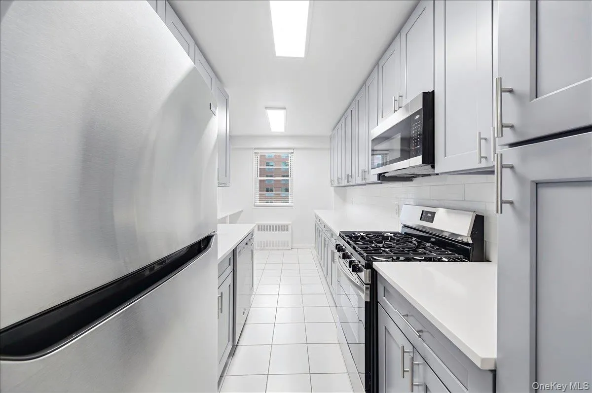 Kitchen with stainless steel appliances, gray cabinetry, light tile patterned flooring, and radiator Kitchen with stainless steel appliances, gray cabinetry, light tile patterned flooring, and radiator