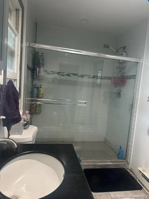 Bathroom featuring vanity, a stall shower, a baseboard heating unit, and light tile patterned flooring Bathroom featuring vanity, a stall shower, a baseboard heating unit, and light tile patterned flooring