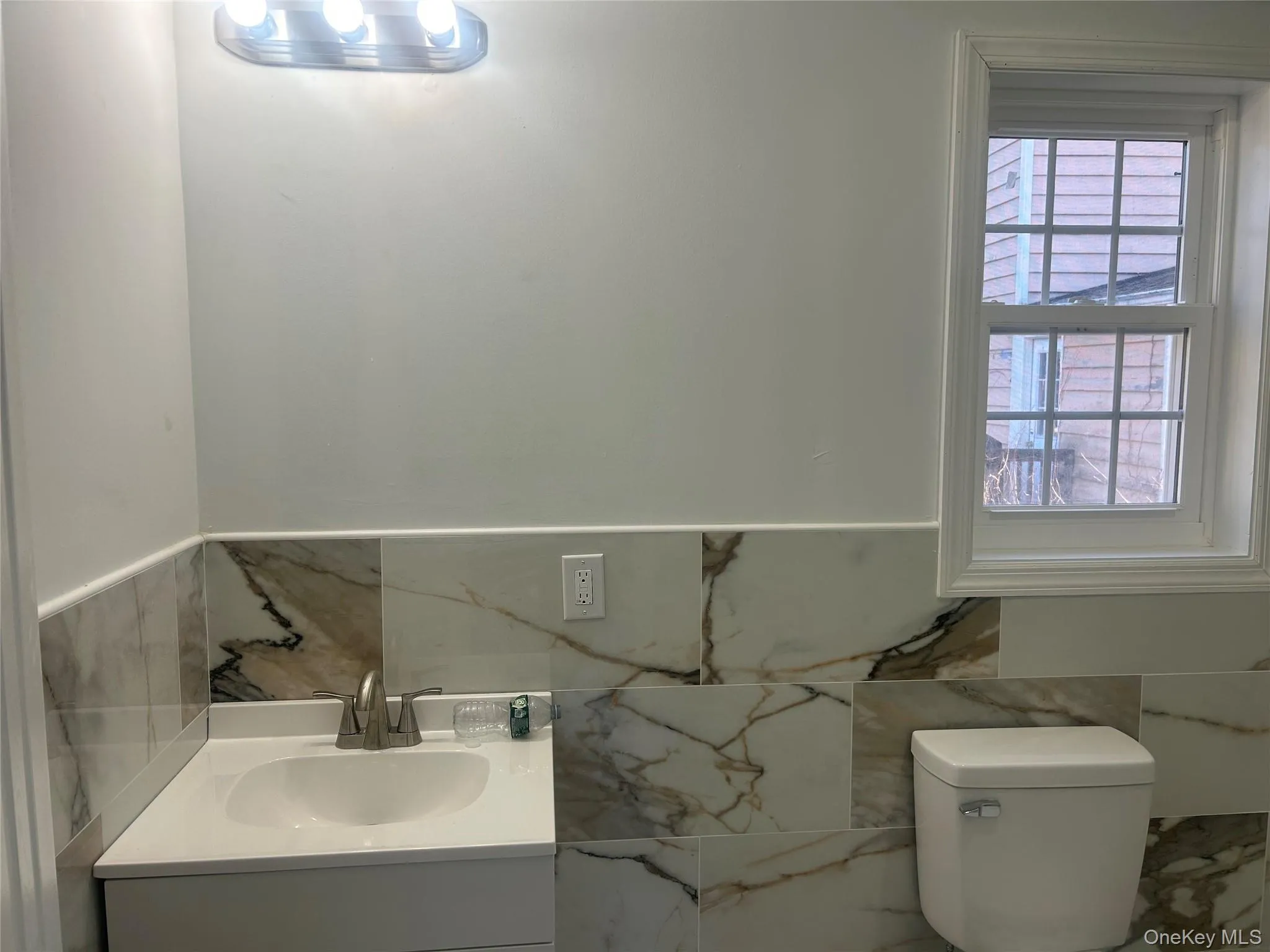Half bathroom featuring vanity, tile walls, and wainscoting Half bathroom featuring vanity, tile walls, and wainscoting