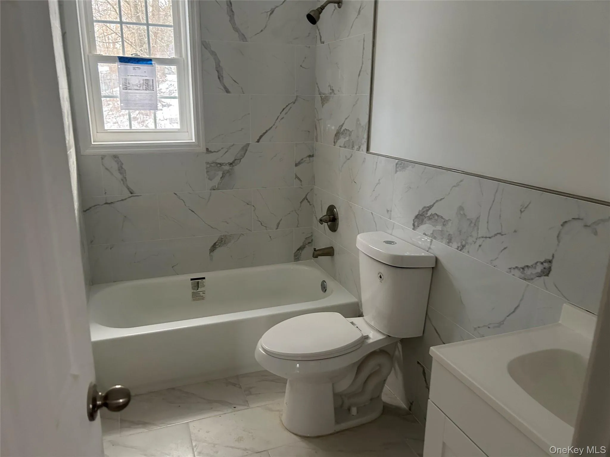 Bathroom with vanity, tile walls, light marble finish floors, and shower / bathtub combination Bathroom with vanity, tile walls, light marble finish floors, and shower / bathtub combination