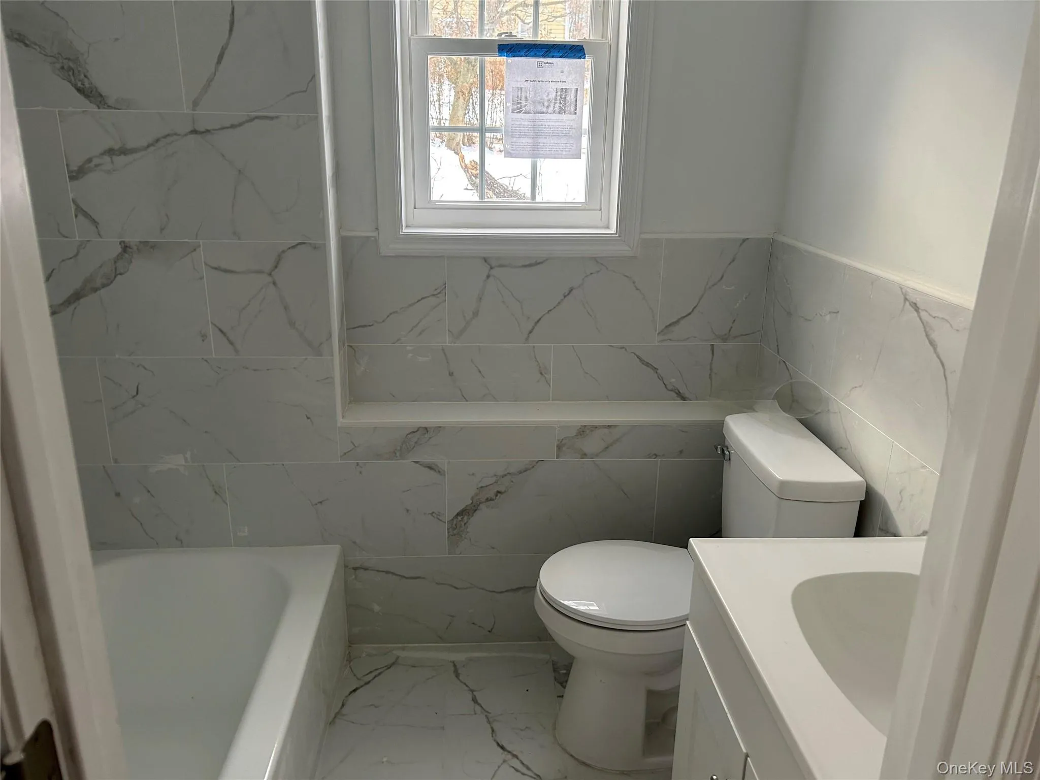 Full bathroom featuring light marble finish flooring, tile walls, vanity, wainscoting, and a bathtub Full bathroom featuring light marble finish flooring, tile walls, vanity, wainscoting, and a bathtub