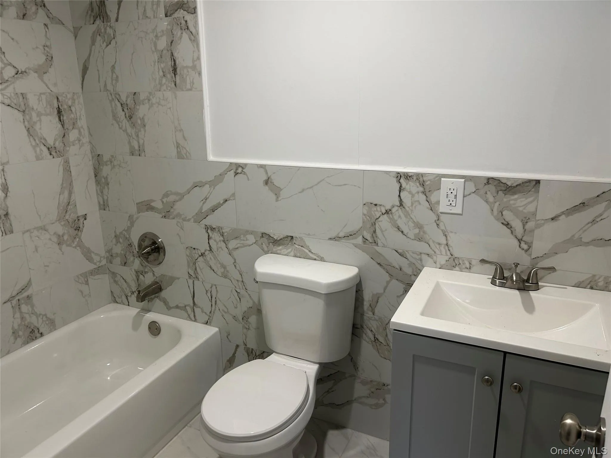 Bathroom featuring tile walls, marble finish flooring, vanity, shower / tub combination, and a wainscoted wall Bathroom featuring tile walls, marble finish flooring, vanity, shower / tub combination, and a wainscoted wall