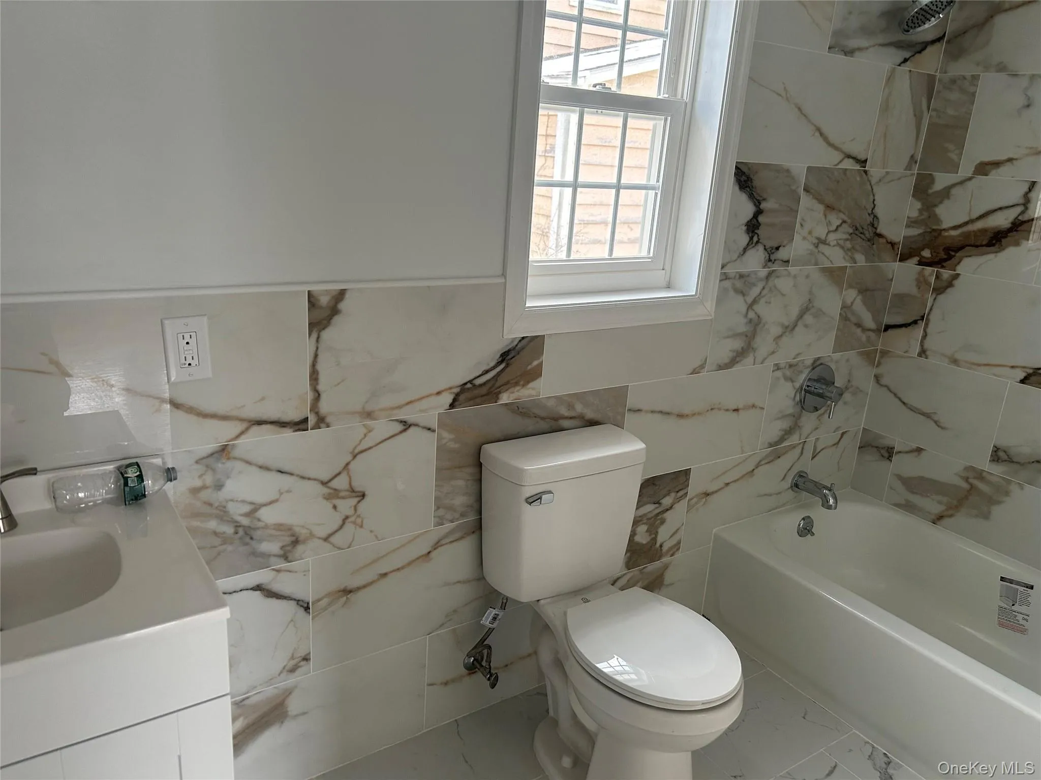 Bathroom with vanity, marble look tile flooring, tile walls, and shower / washtub combination Bathroom with vanity, marble look tile flooring, tile walls, and shower / washtub combination