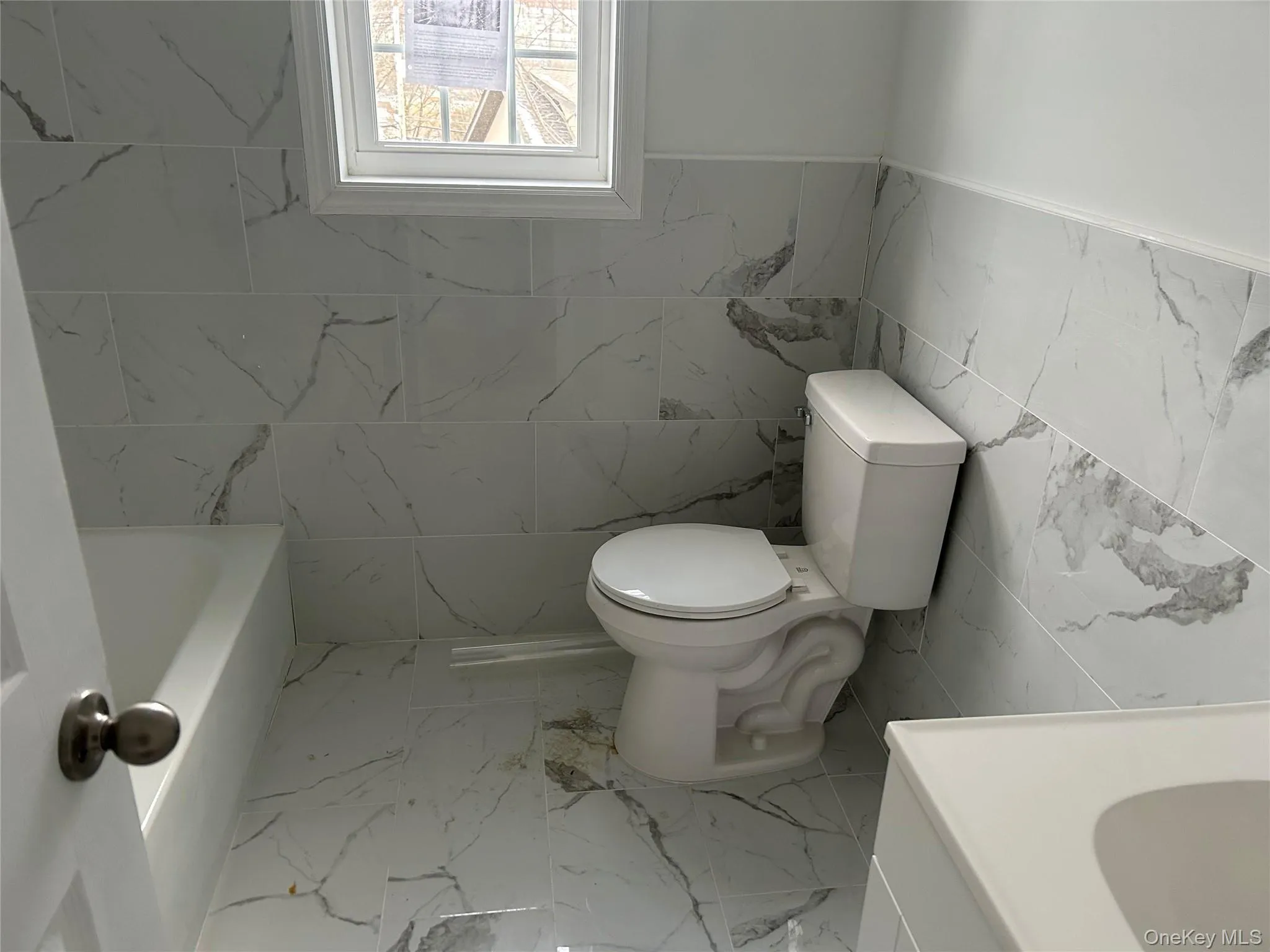 Bathroom with tile walls, light marble finish floors, vanity, a bath, and a wainscoted wall Bathroom with tile walls, light marble finish floors, vanity, a bath, and a wainscoted wall