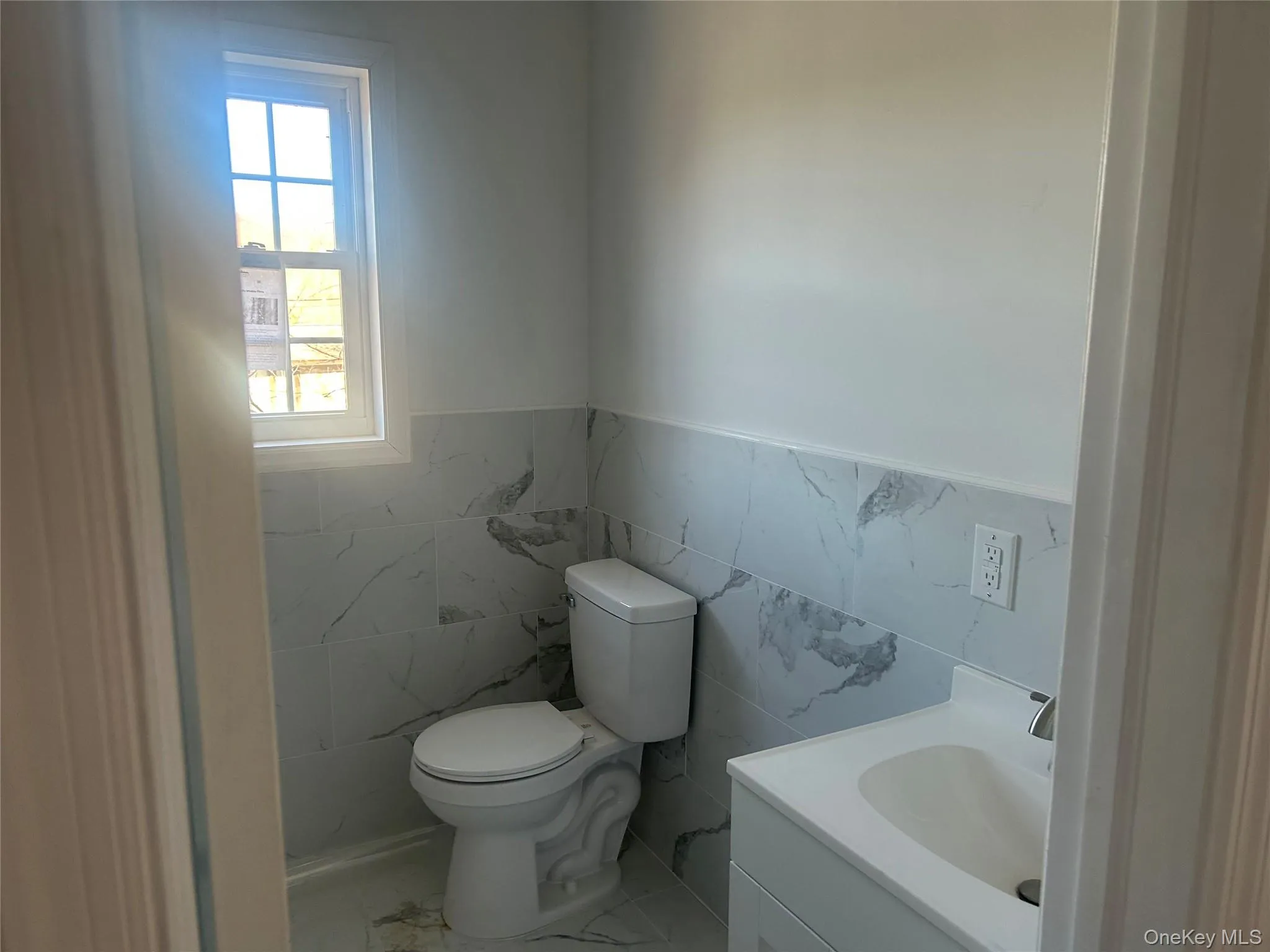 Bathroom featuring wainscoting, tile walls, vanity, and marble look tile flooring Bathroom featuring wainscoting, tile walls, vanity, and marble look tile flooring