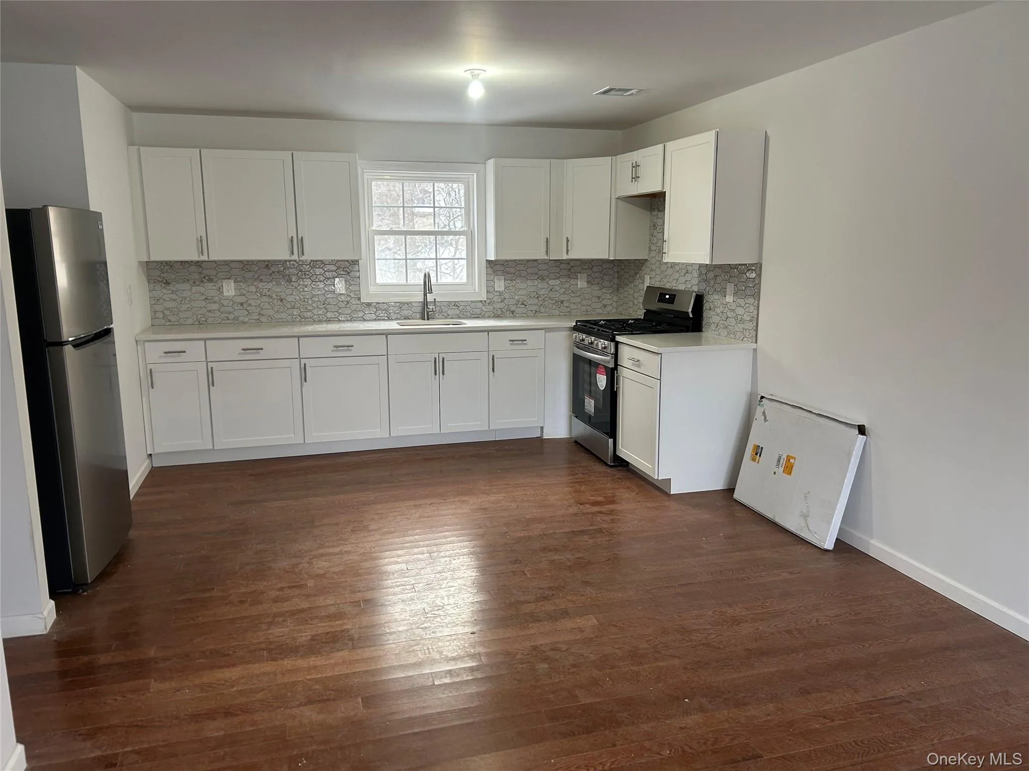 Kitchen with stainless steel appliances, white cabinetry, dark wood-style flooring, and decorative backsplash Kitchen with stainless steel appliances, white cabinetry, dark wood-style flooring, and decorative backsplash