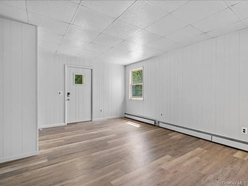 Empty room featuring wood finished floors, a paneled ceiling, baseboards, and baseboard heating Empty room featuring wood finished floors, a paneled ceiling, baseboards, and baseboard heating