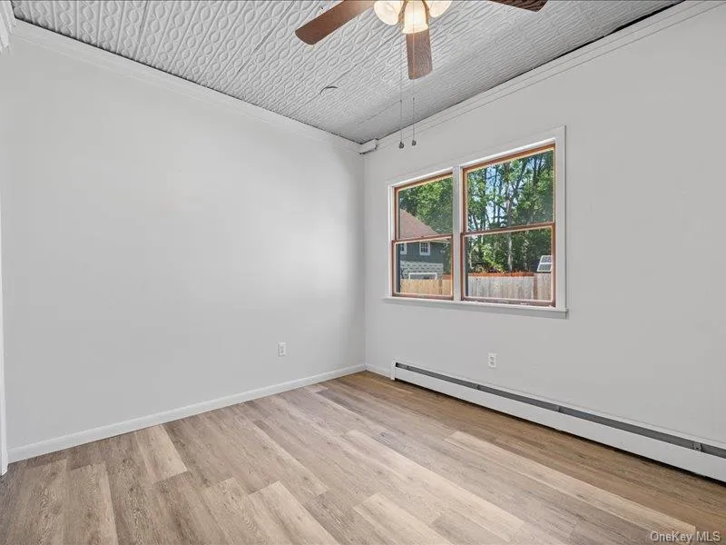 Unfurnished room with baseboard heating, a ceiling fan, light wood-style floors, crown molding, and baseboards Unfurnished room with baseboard heating, a ceiling fan, light wood-style floors, crown molding, and baseboards