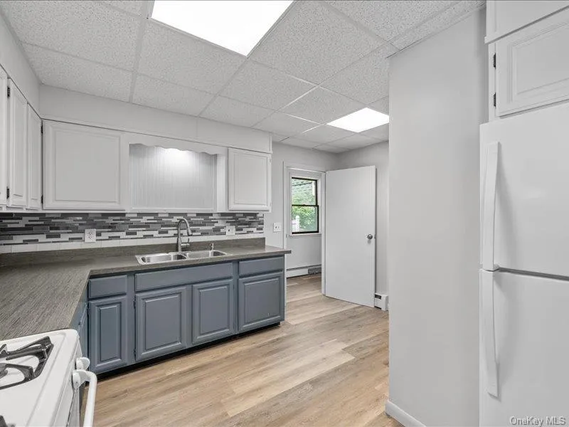 Kitchen with freestanding refrigerator, range, a sink, a drop ceiling, and white cabinetry Kitchen with freestanding refrigerator, range, a sink, a drop ceiling, and white cabinetry