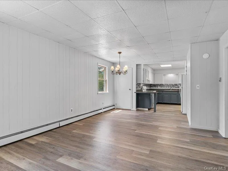 Unfurnished living room featuring a chandelier, baseboard heating, wood finished floors, a drop ceiling, and a sink Unfurnished living room featuring a chandelier, baseboard heating, wood finished floors, a drop ceiling, and a sink