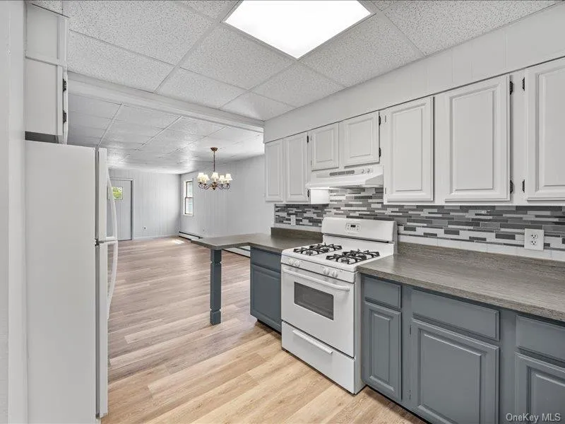 Kitchen with white appliances, under cabinet range hood, a drop ceiling, a chandelier, and gray cabinets Kitchen with white appliances, under cabinet range hood, a drop ceiling, a chandelier, and gray cabinets