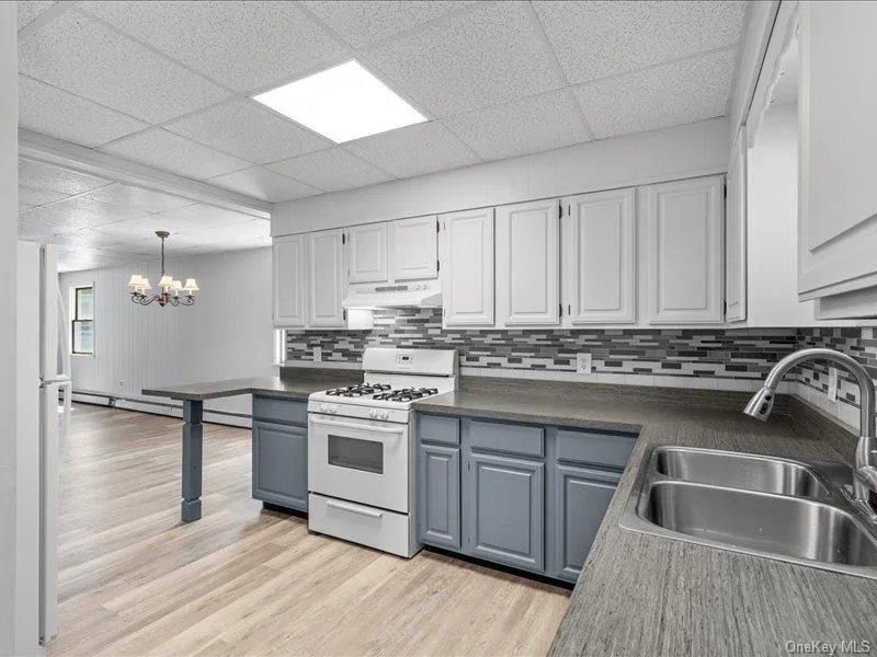 Kitchen featuring white gas range oven, a sink, a chandelier, dark countertops, and blue cabinets Kitchen featuring white gas range oven, a sink, a chandelier, dark countertops, and blue cabinets