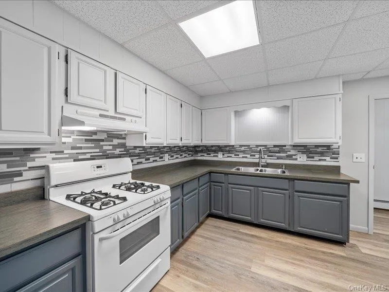Kitchen with gas range gas stove, under cabinet range hood, a sink, dark countertops, and a paneled ceiling Kitchen with gas range gas stove, under cabinet range hood, a sink, dark countertops, and a paneled ceiling