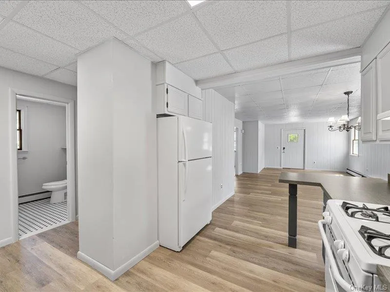 Kitchen with white appliances, baseboard heating, a drop ceiling, light wood-style floors, and white cabinets Kitchen with white appliances, baseboard heating, a drop ceiling, light wood-style floors, and white cabinets