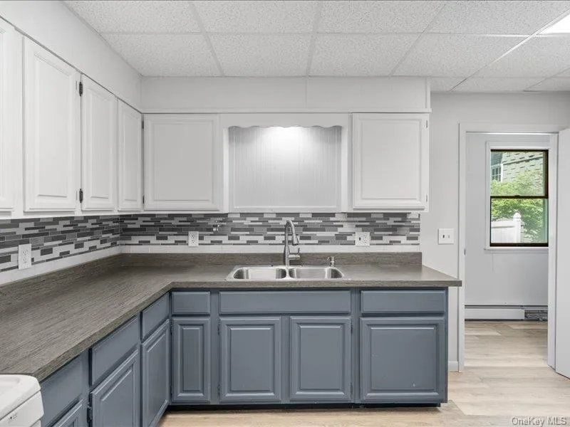 Kitchen with a sink, a drop ceiling, a baseboard heating unit, and white cabinets Kitchen with a sink, a drop ceiling, a baseboard heating unit, and white cabinets
