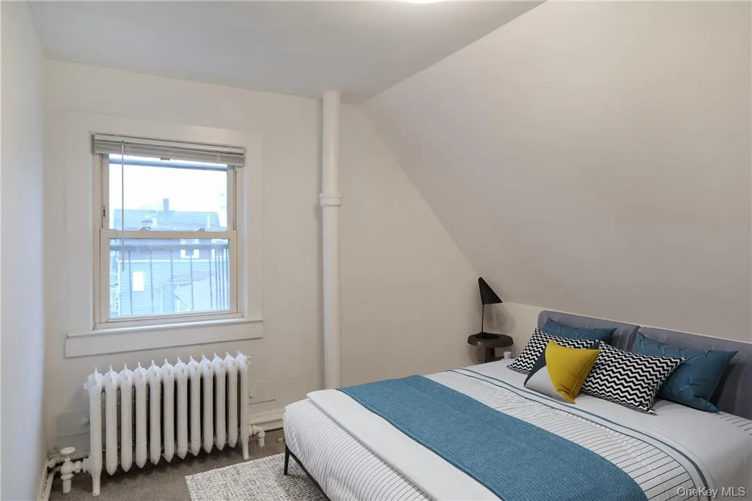 Bedroom with radiator, carpet flooring, and vaulted ceiling Bedroom with radiator, carpet flooring, and vaulted ceiling