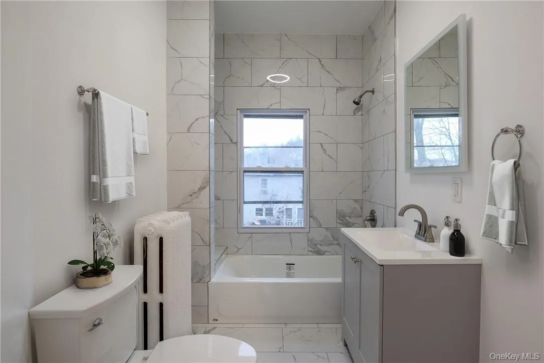 Bathroom with vanity, radiator, tub / shower combination, and light marble finish flooring Bathroom with vanity, radiator, tub / shower combination, and light marble finish flooring