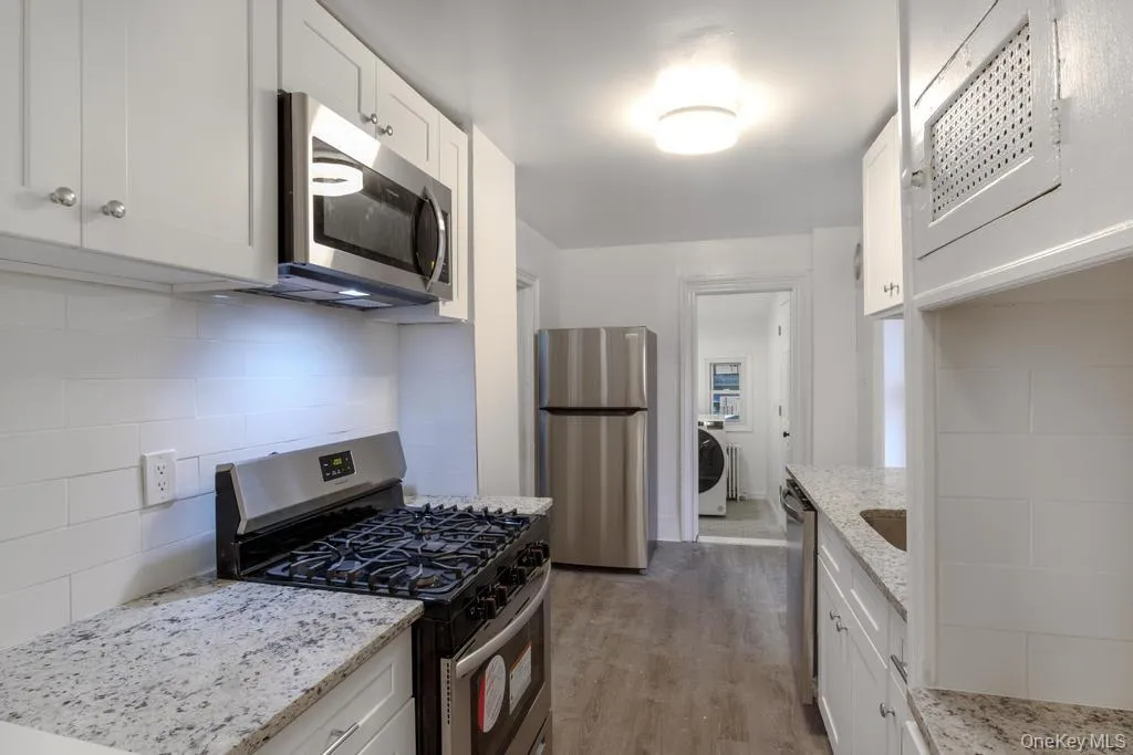 Kitchen with stainless steel appliances, white cabinetry, backsplash, light stone counters, and light wood finished floors Kitchen with stainless steel appliances, white cabinetry, backsplash, light stone counters, and light wood finished floors