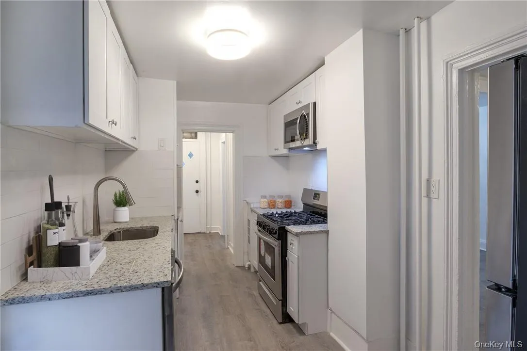 Kitchen with stainless steel appliances, white cabinetry, light stone counters, light wood finished floors, and backsplash Kitchen with stainless steel appliances, white cabinetry, light stone counters, light wood finished floors, and backsplash