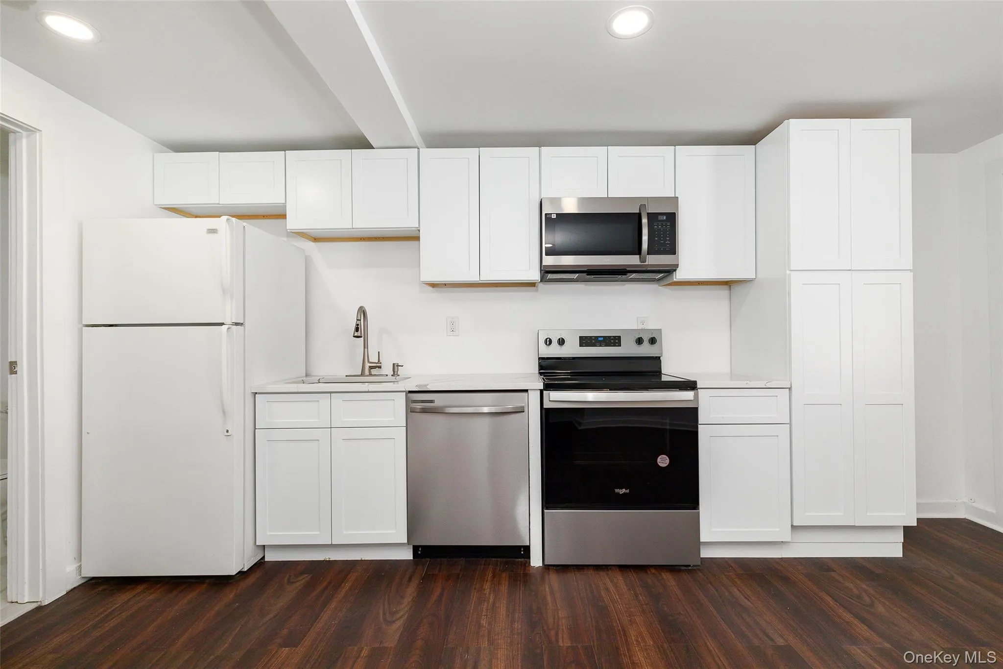 Kitchen featuring appliances with stainless steel finishes, dark wood-type flooring, light quartz countertops, white cabinetry, and a sink Kitchen featuring appliances with stainless steel finishes, dark wood-type flooring, light quartz countertops, white cabinetry, and a sink