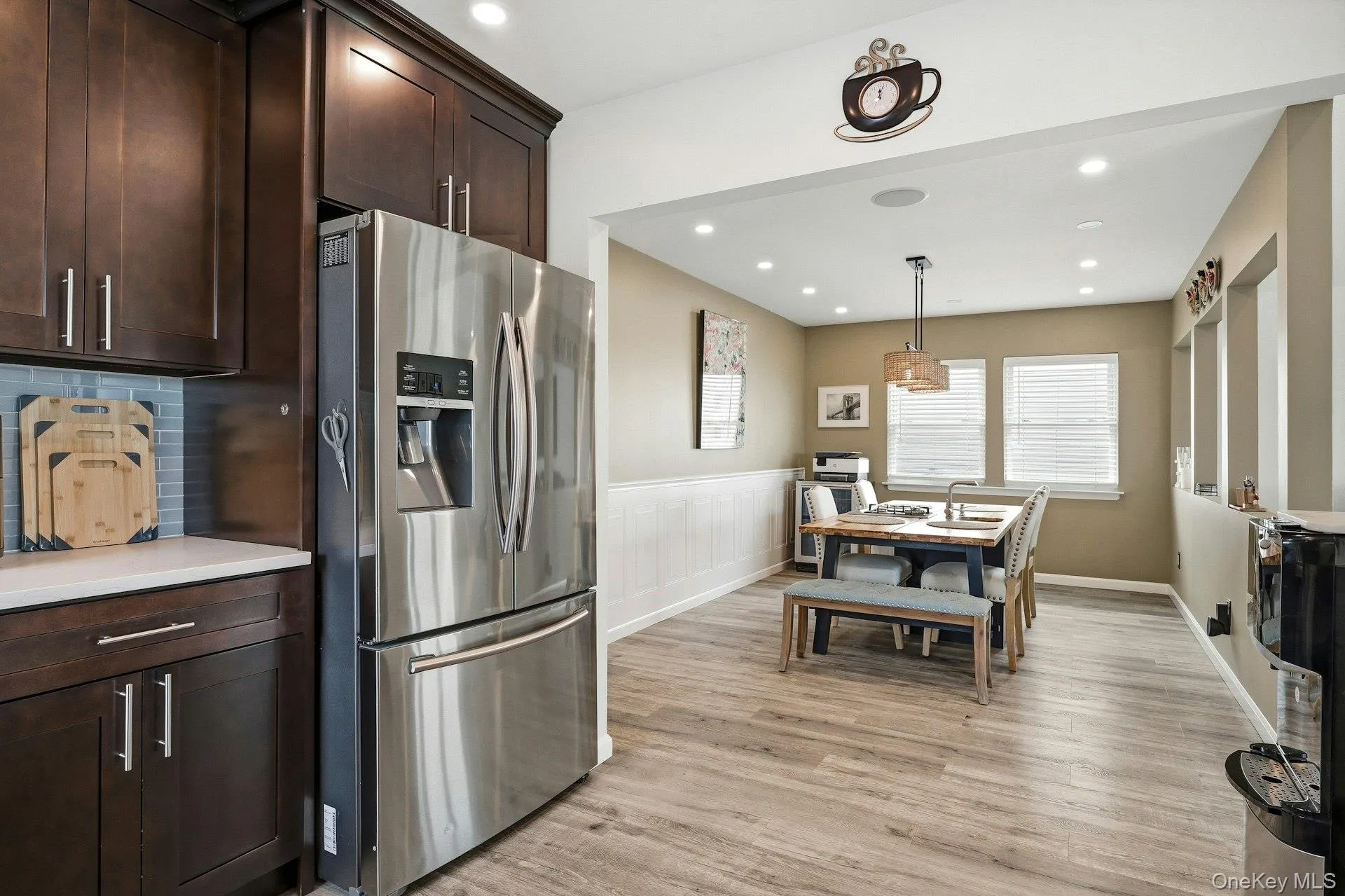 Kitchen with stainless steel fridge with ice dispenser, dark wood finish cabinets, a wainscoted wall, light wood finished floors, and hanging light fixtures Kitchen with stainless steel fridge with ice dispenser, dark wood finish cabinets, a wainscoted wall, light wood finished floors, and hanging light fixtures
