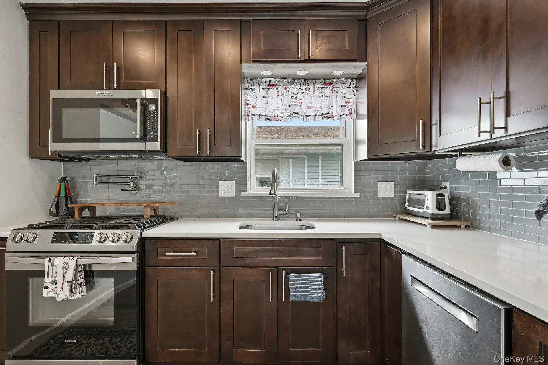 Kitchen with stainless steel appliances, dark wood finish cabinets, light stone counters, and decorative backsplash Kitchen with stainless steel appliances, dark wood finish cabinets, light stone counters, and decorative backsplash
