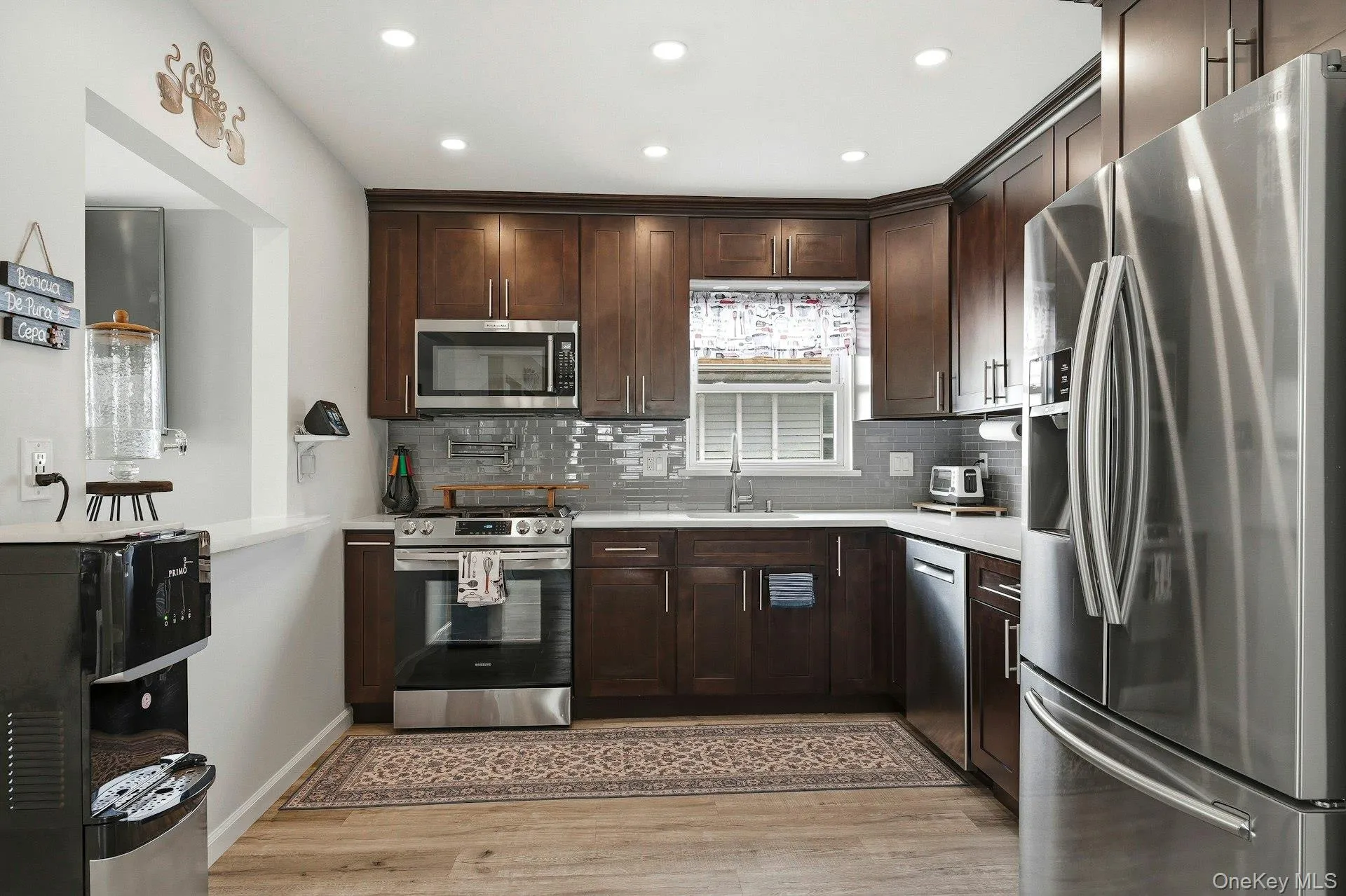 Kitchen with stainless steel appliances, dark wood finish cabinetry, recessed lighting, light wood finished floors, and tasteful backsplash Kitchen with stainless steel appliances, dark wood finish cabinetry, recessed lighting, light wood finished floors, and tasteful backsplash
