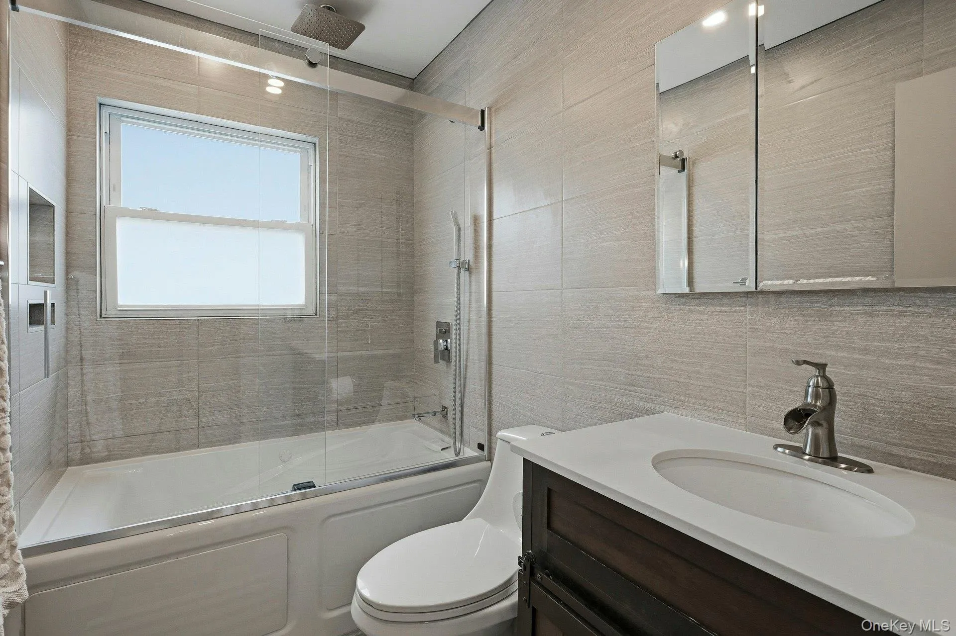 Bathroom featuring tile walls, vanity, and a combined bath / shower with rainfall shower Bathroom featuring tile walls, vanity, and a combined bath / shower with rainfall shower