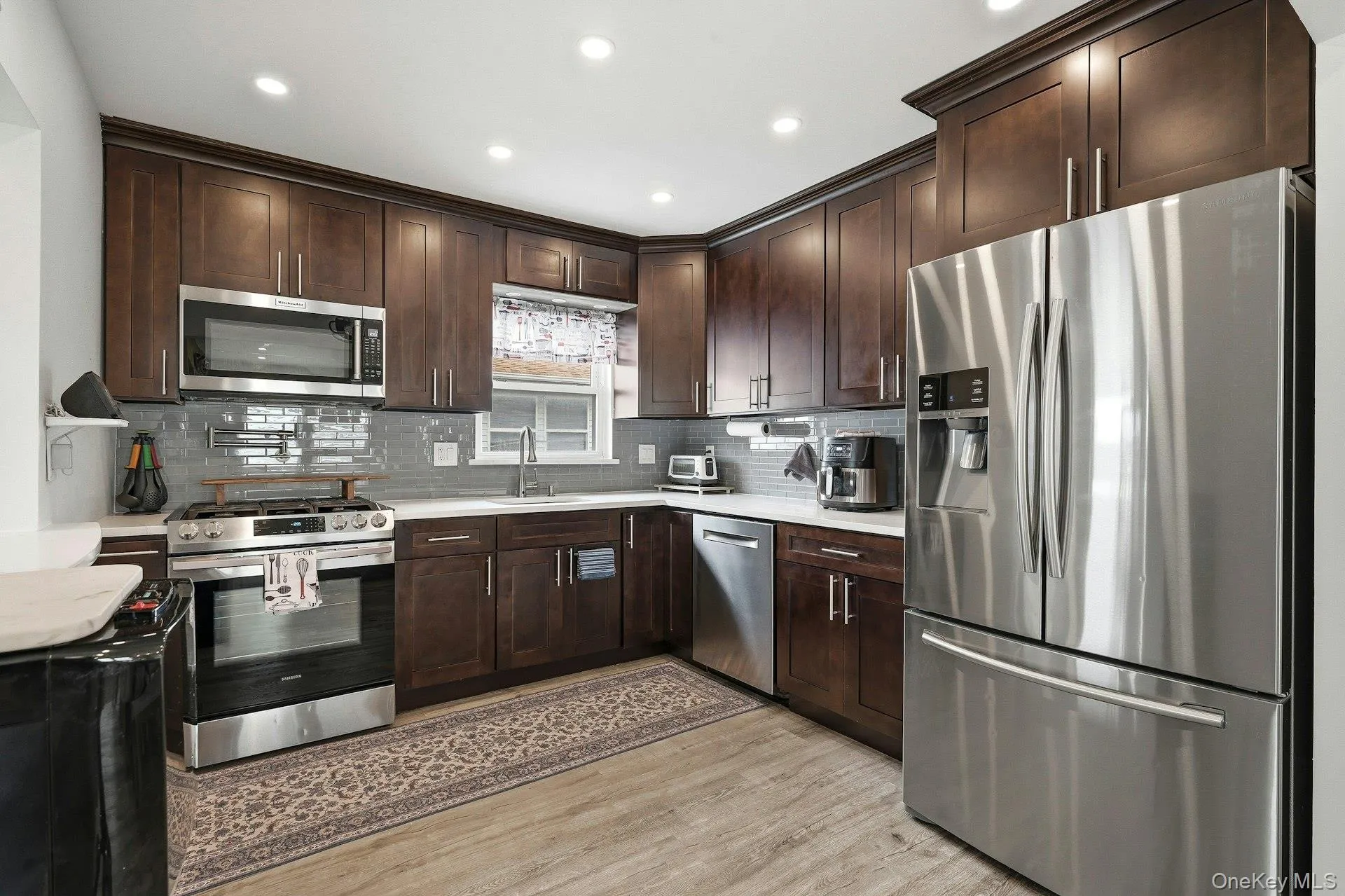 Kitchen featuring stainless steel appliances, dark wood finish cabinets, light wood-style floors, recessed lighting, and decorative backsplash Kitchen featuring stainless steel appliances, dark wood finish cabinets, light wood-style floors, recessed lighting, and decorative backsplash