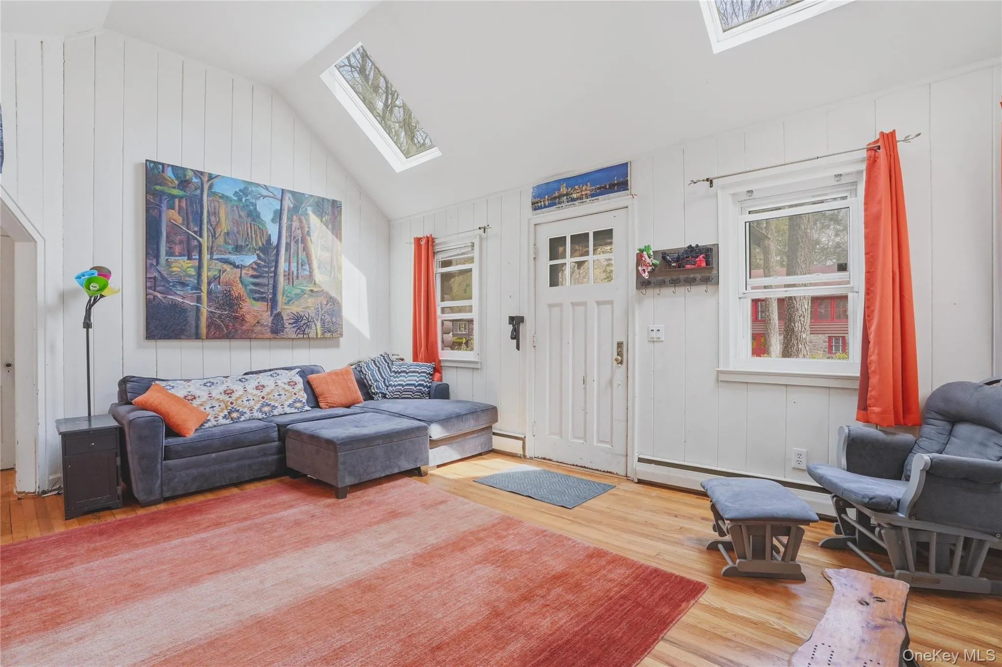 Living area featuring hardwood floors, white vertical paneling on the walls, and a vaulted ceiling with skylights Living area featuring hardwood floors, white vertical paneling on the walls, and a vaulted ceiling with skylights