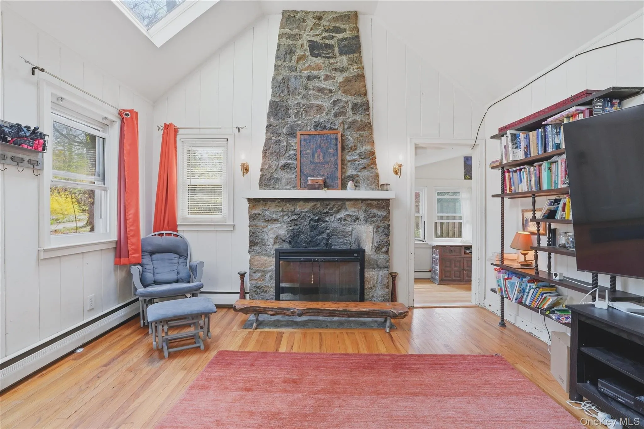 The living area features hardwood floors, a stone fireplace with hearth, and white paneled walls The living area features hardwood floors, a stone fireplace with hearth, and white paneled walls