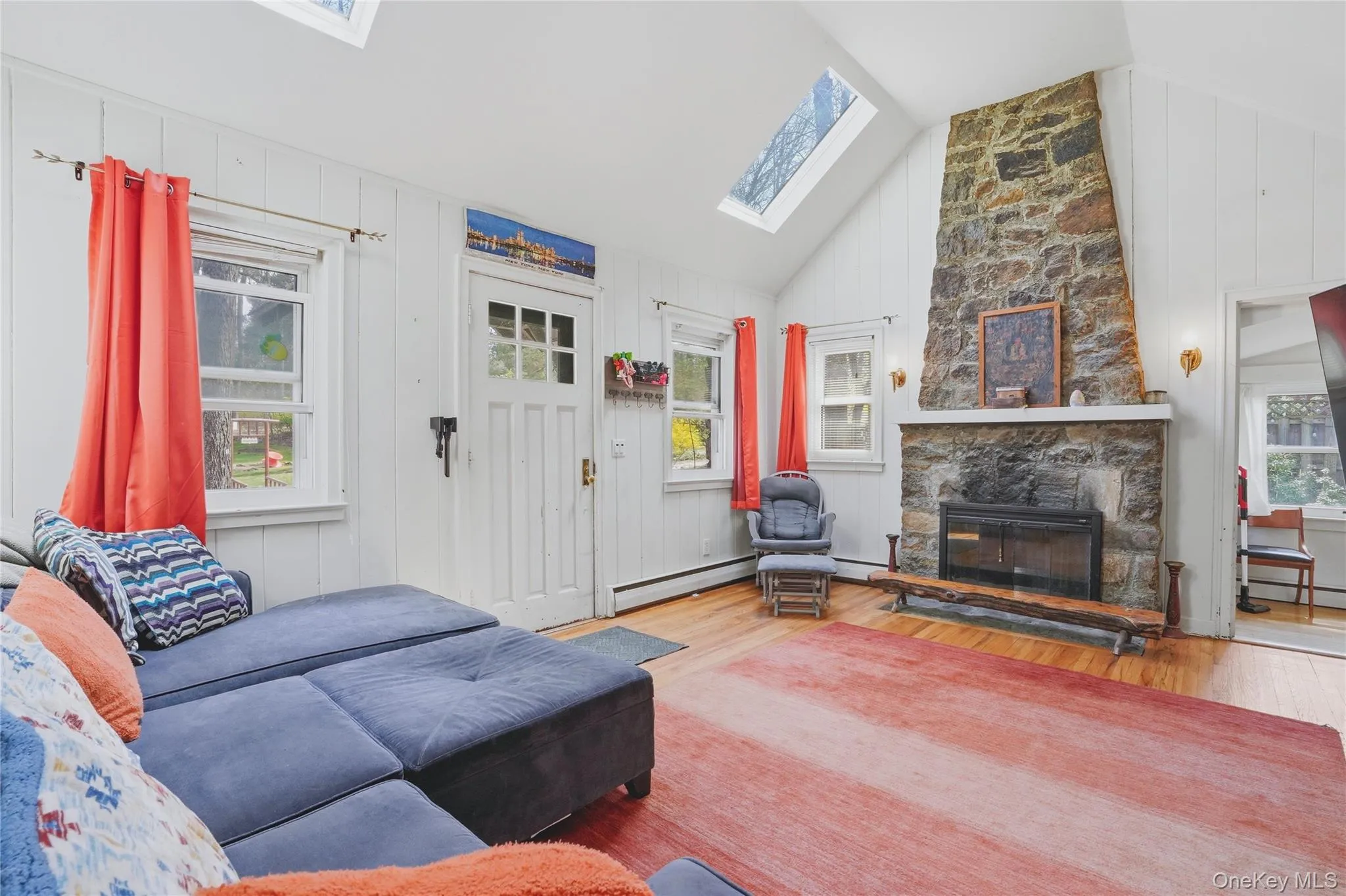 The living room features a stone fireplace, hardwood flooring, and skylights The living room features a stone fireplace, hardwood flooring, and skylights