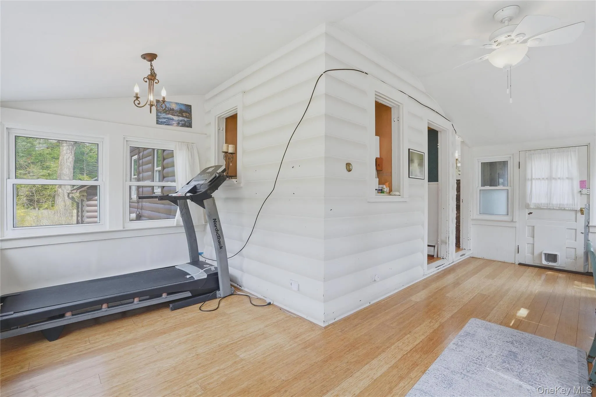 This bright room features light wood flooring, white paneled walls, and a white ceiling fan This bright room features light wood flooring, white paneled walls, and a white ceiling fan
