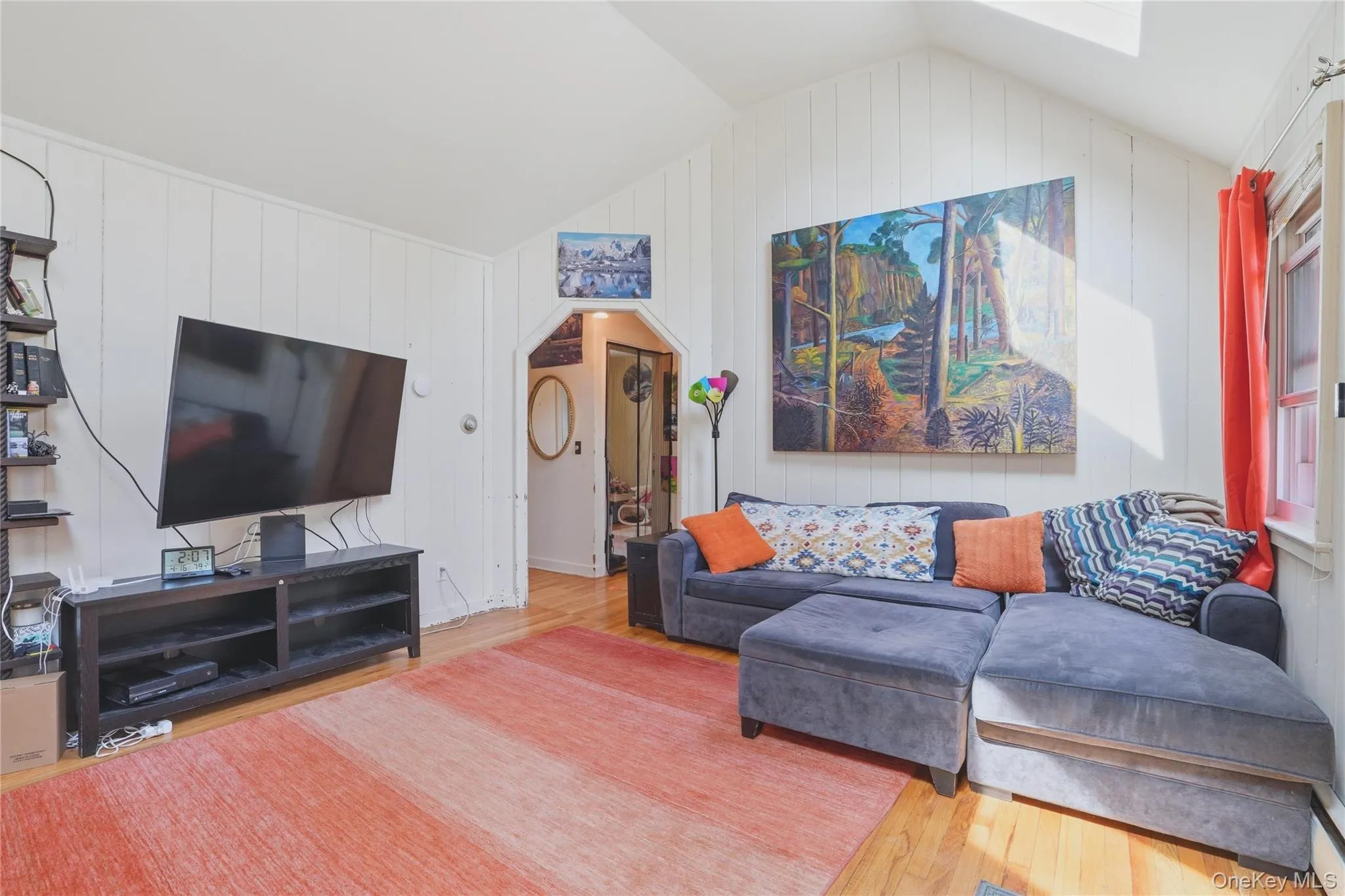 Living area featuring hardwood floors, a vaulted ceiling with skylight, and a doorway with an arched frame Living area featuring hardwood floors, a vaulted ceiling with skylight, and a doorway with an arched frame